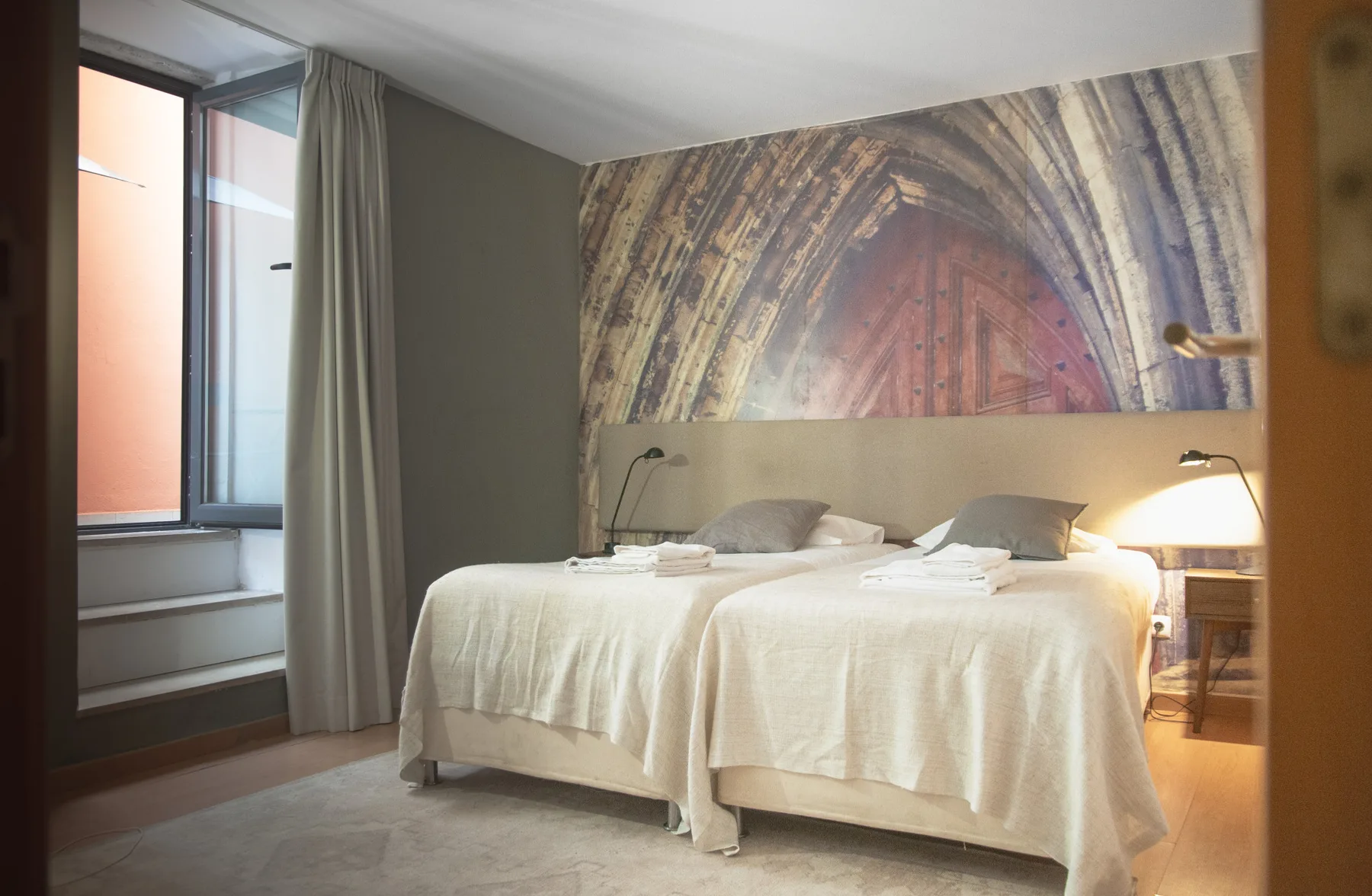 Dormitorio con dos camas bajo un gran mural de un arco.