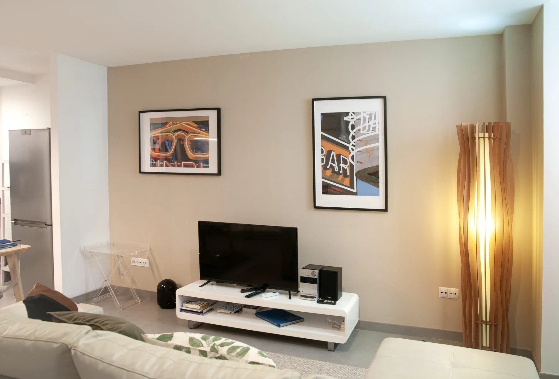 Una sala de estar con un televisor sobre un mueble bajo y cuadros en la pared.