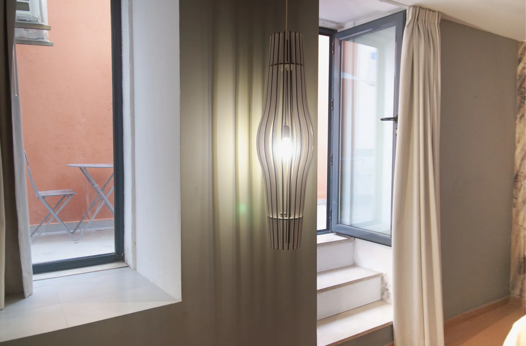 A room with a sculptural hanging light beside open windows and a small terrace.