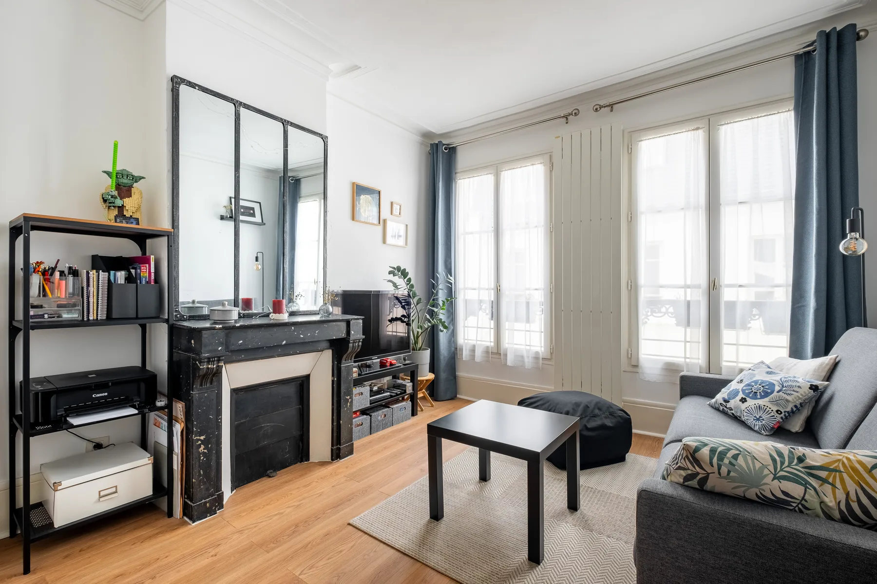 A bright living room with a fireplace, seating, and tall curtained windows.