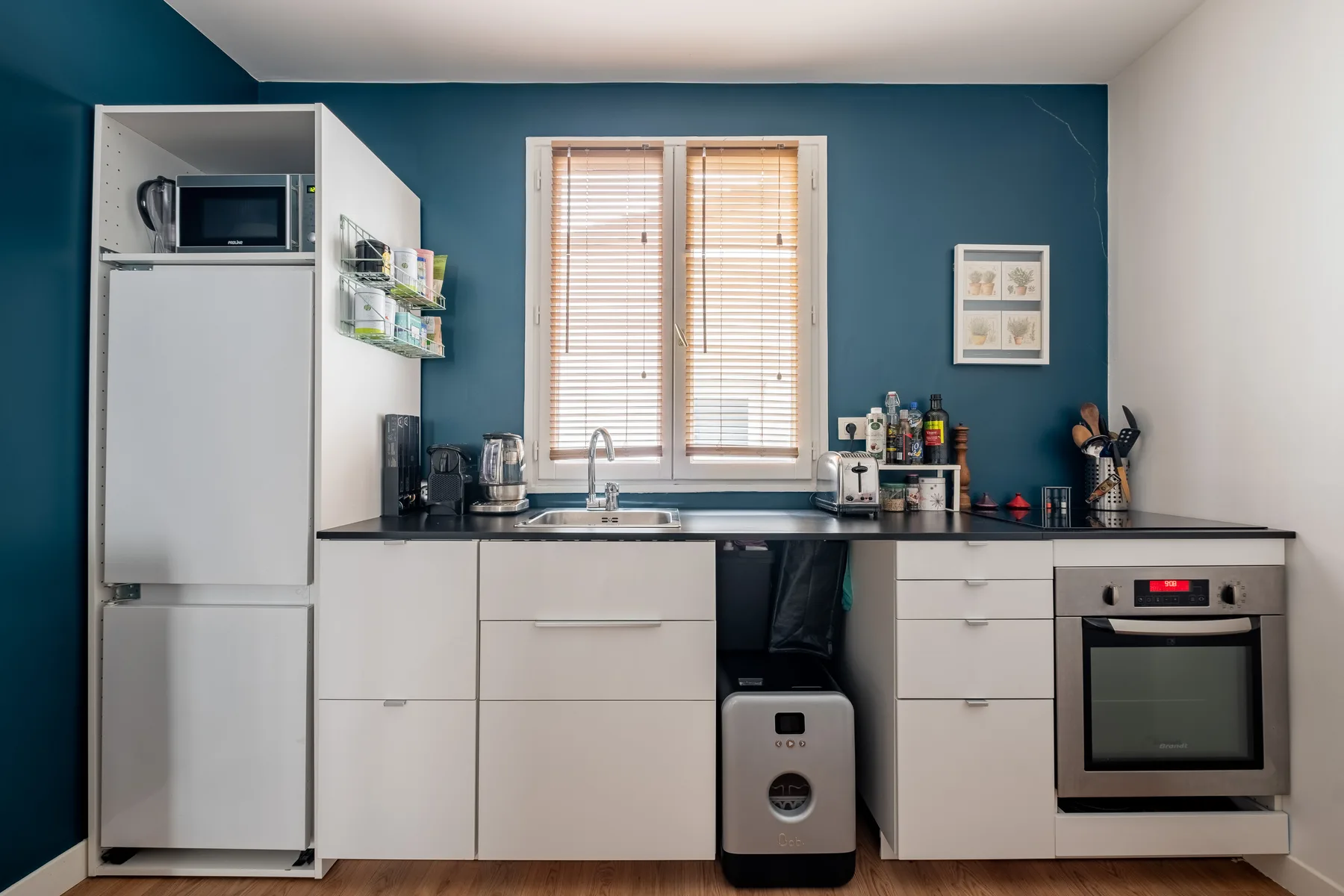 Una cocina compacta con gabinetes blancos, una encimera y una ventana con persianas.