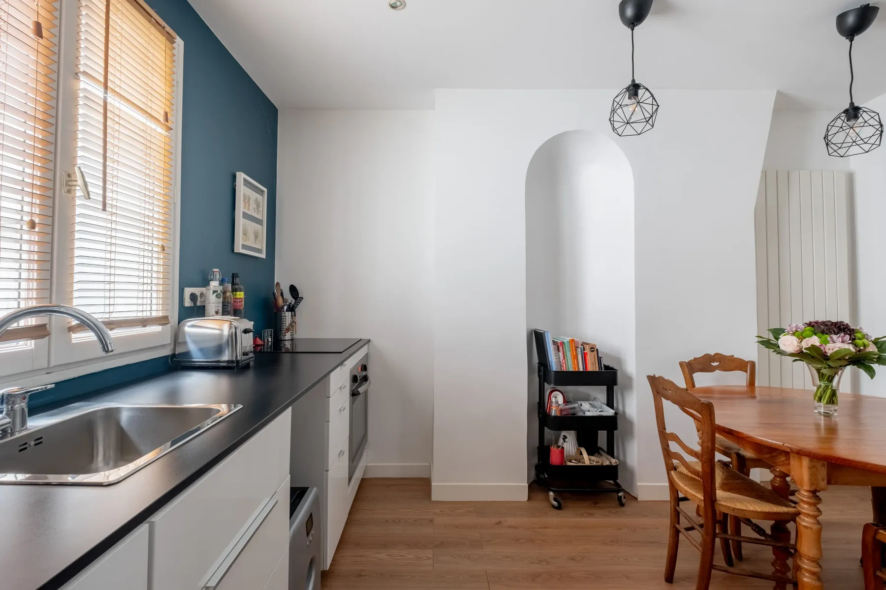 Cocina y comedor con una encimera, una mesa de madera y lámparas colgantes.