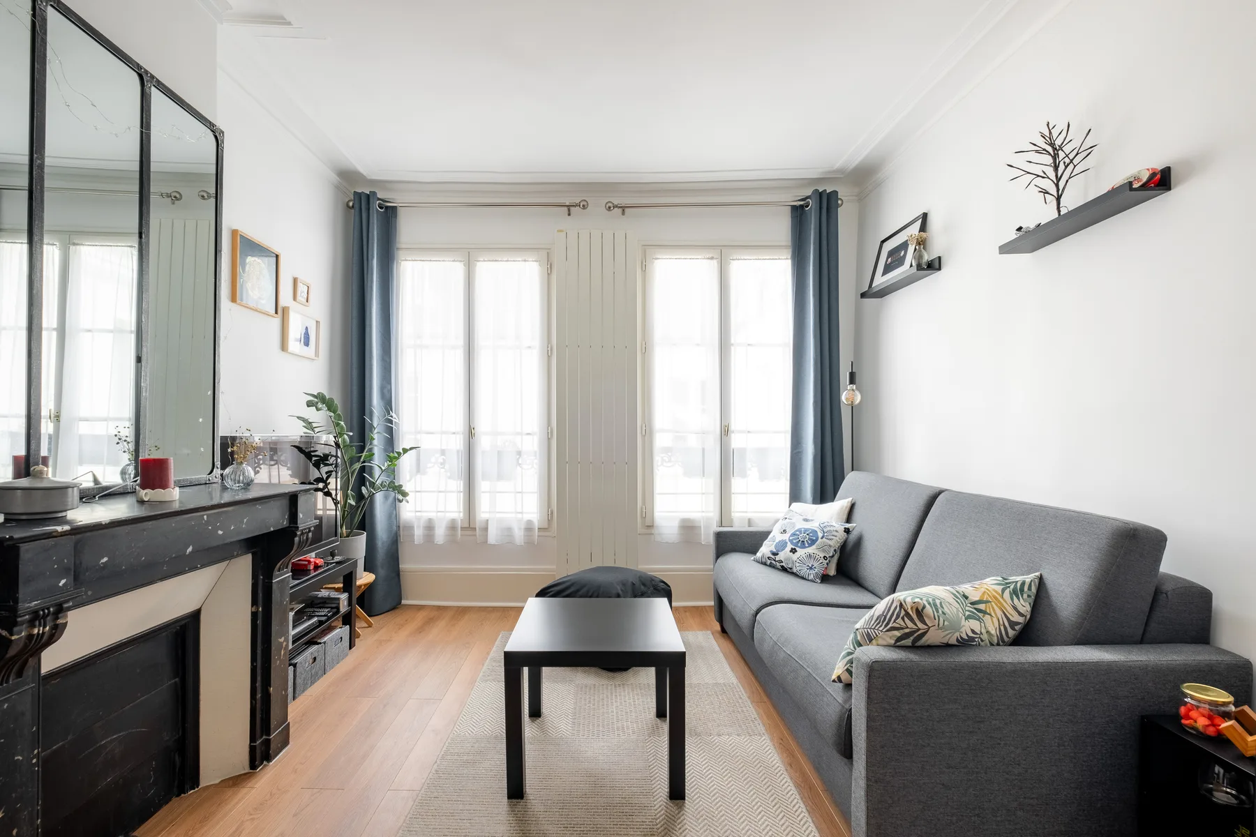 Una sala luminosa con asientos grises, una mesa de centro y ventanas altas.
