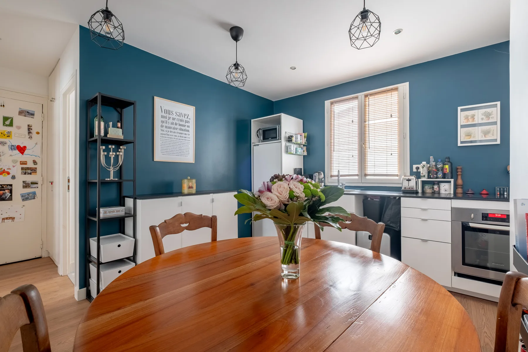 Un comedor con mesa de madera y paredes azules se abre a una cocina.