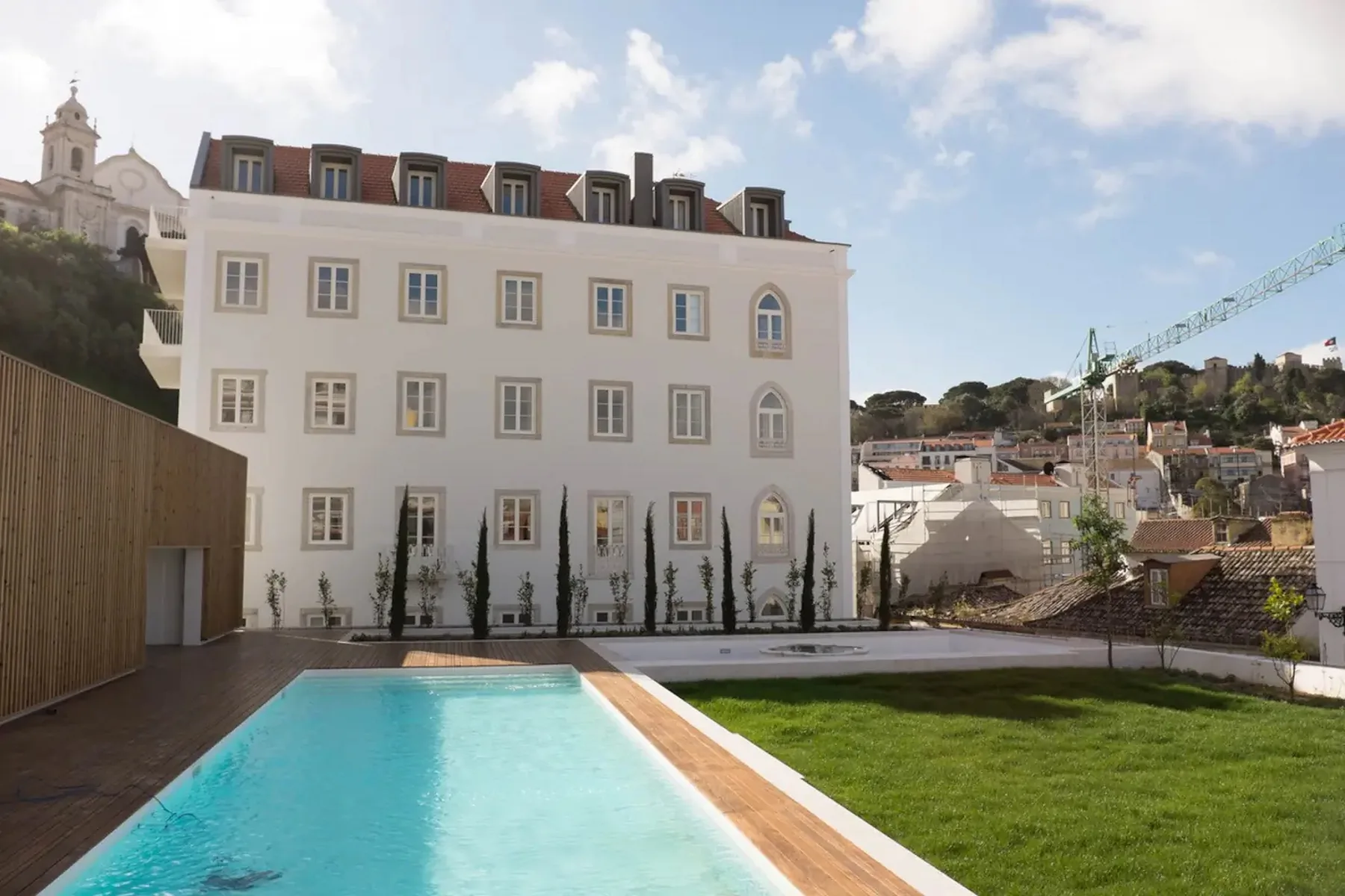 Una piscina en un patio está junto a un césped y un edificio claro de varias plantas.
