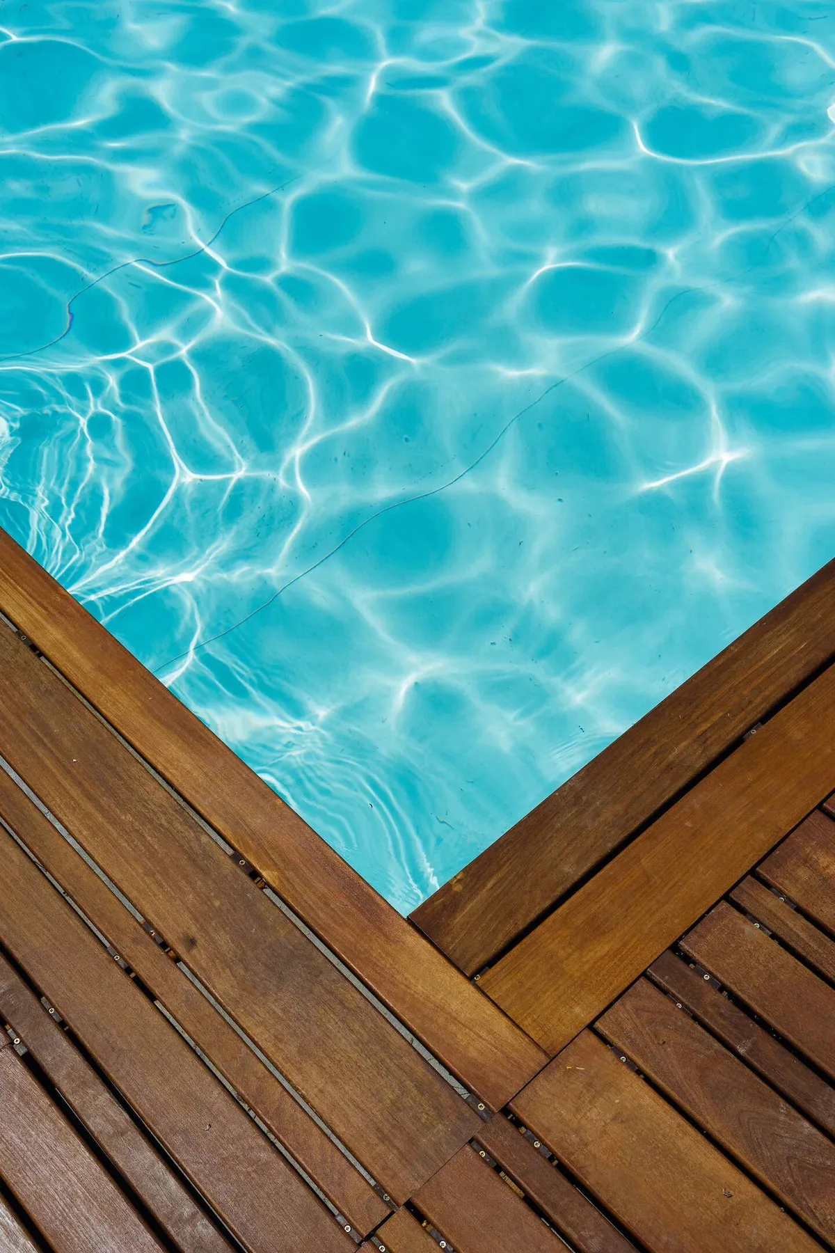 Una piscina de agua azul ondulada bordeada por una tarima de madera.