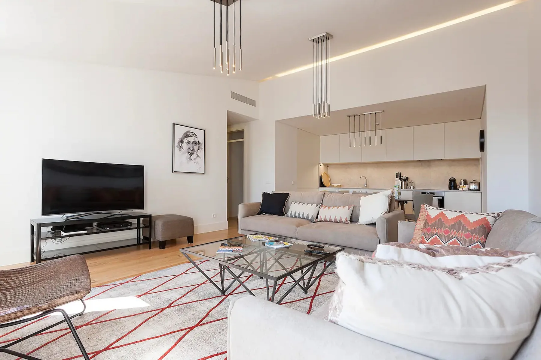 Una sala de estar luminosa con asientos, televisor y cocina abierta.