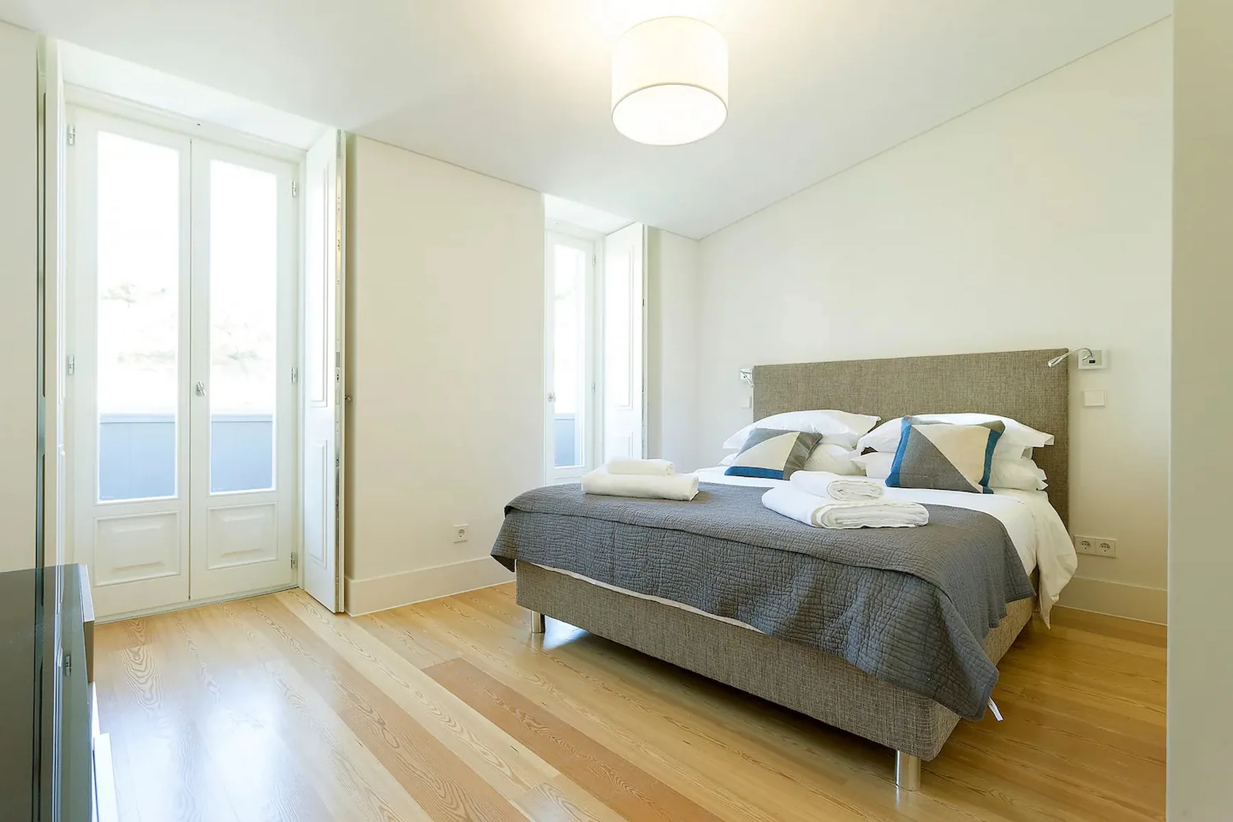 Un dormitorio luminoso con una cama doble y ventanas altas.