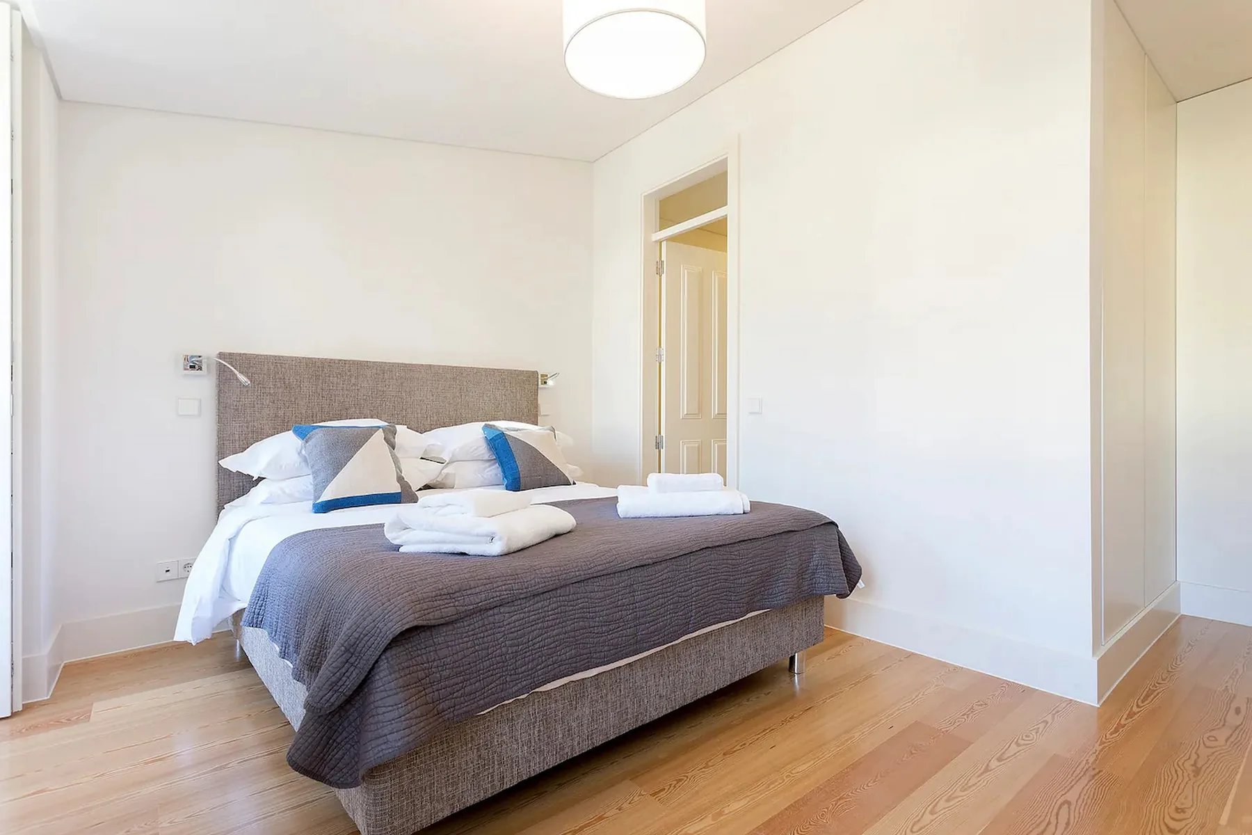 Un dormitorio con una cama, toallas dobladas y suelo de madera clara.