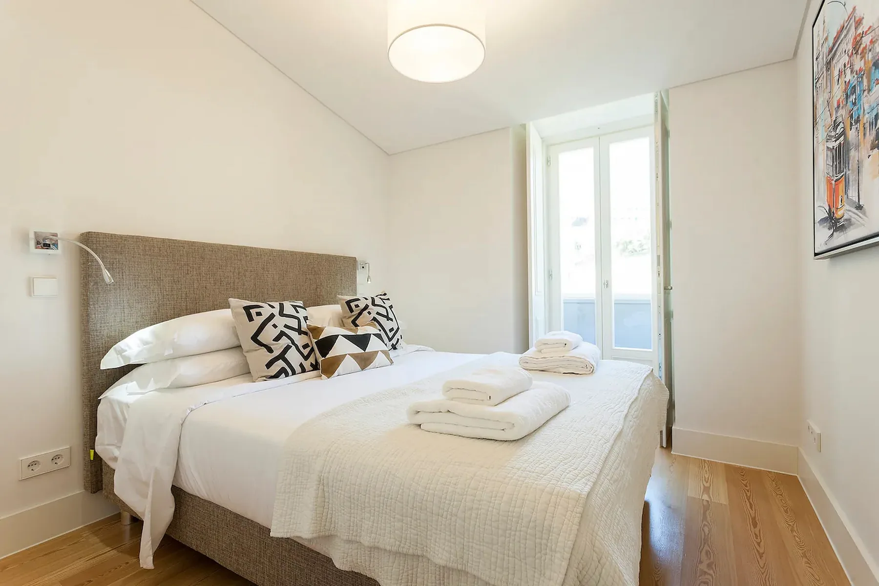 Un dormitorio con una cama doble, cojines estampados y una ventana luminosa.