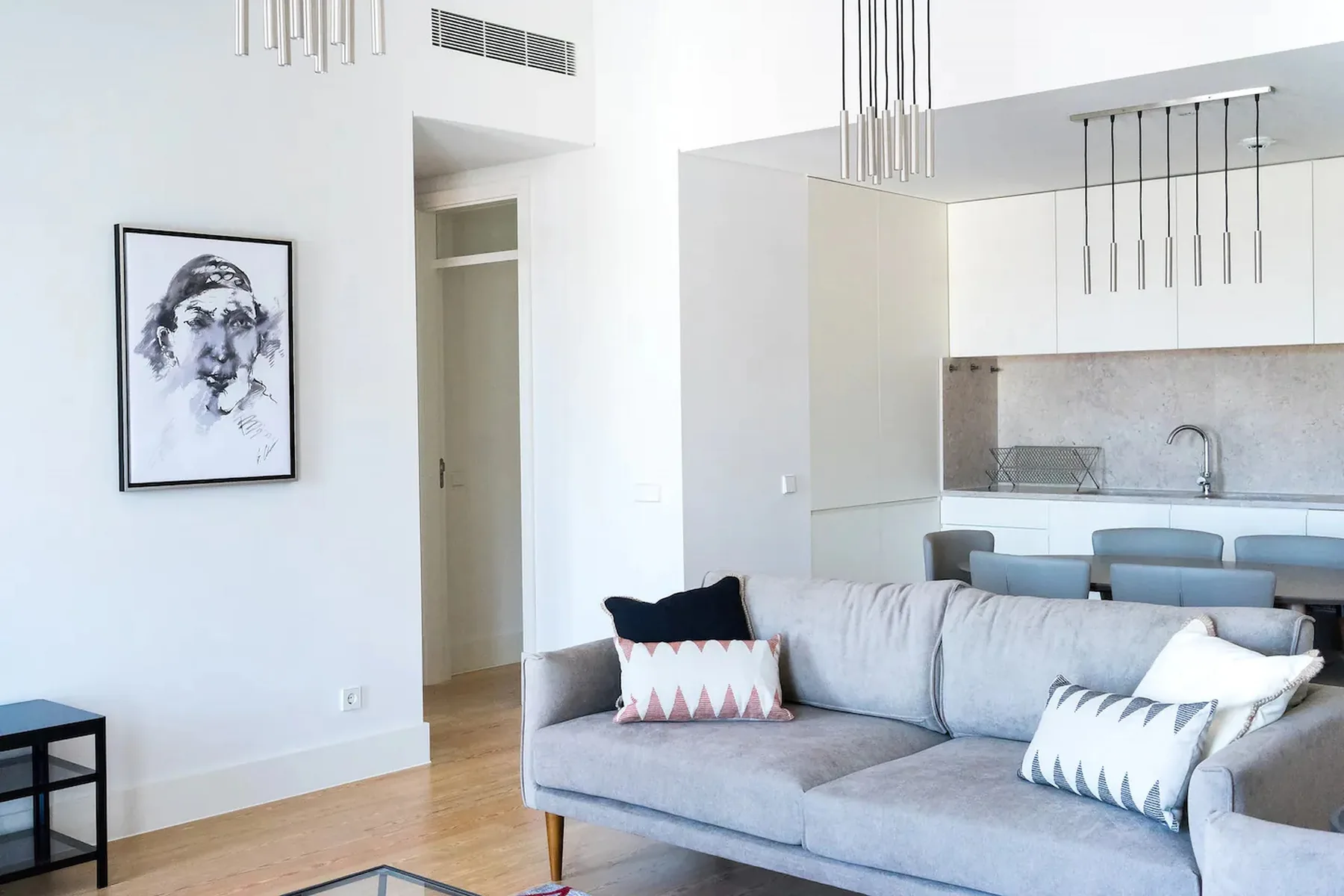 Sala luminosa con asientos grises y una cocina abierta.