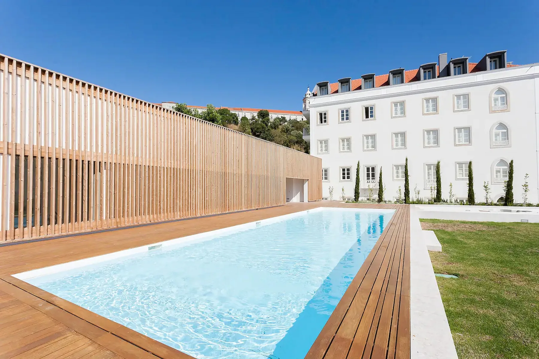 Una piscina al aire libre junto a una terraza de madera y césped.