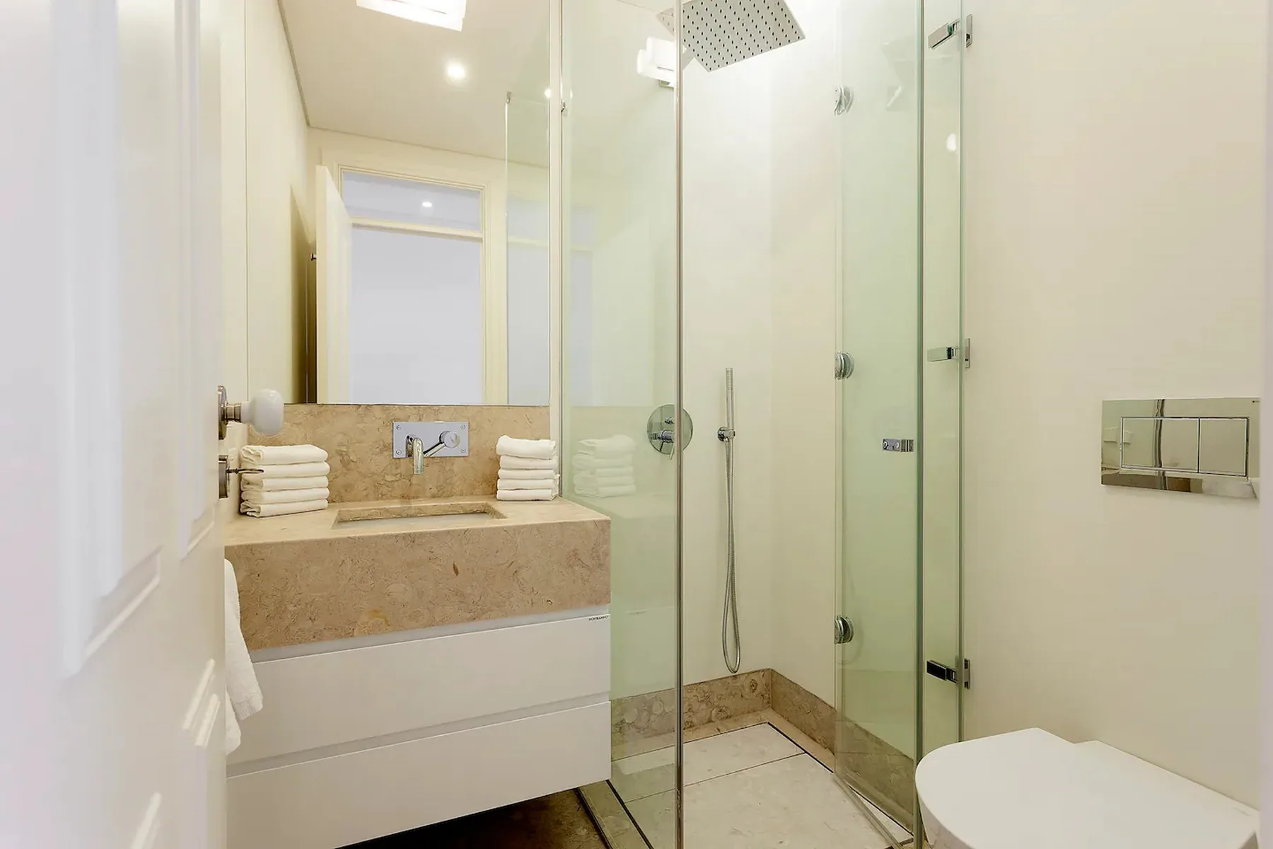 Un baño luminoso con ducha de vidrio y un lavabo con toallas dobladas.