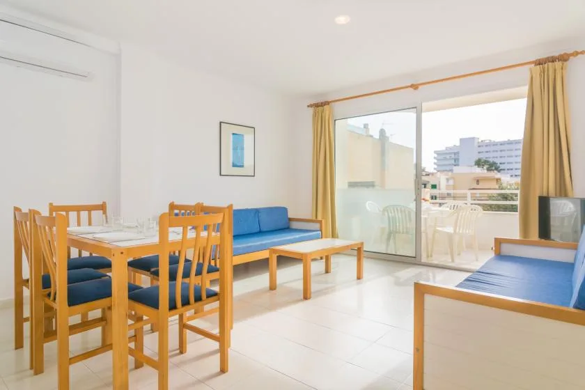 A bright living and dining area has blue seating and large windows opening onto a balcony.