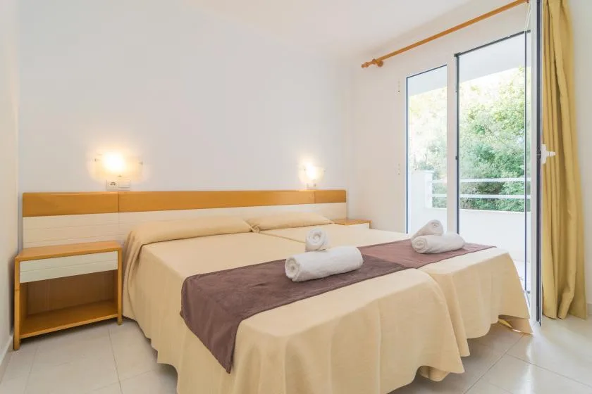 A bright bedroom with two beds and a large window overlooking greenery.