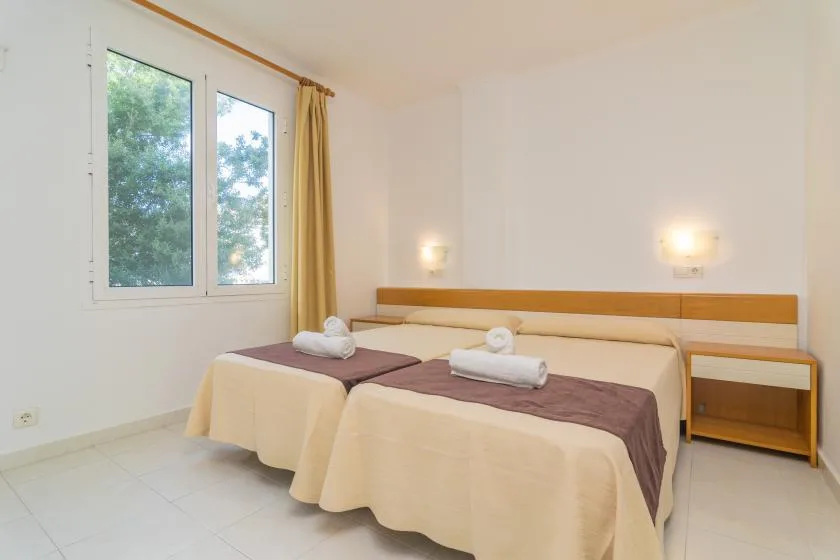 A bright bedroom with two beds arranged side by side beneath a wide window.