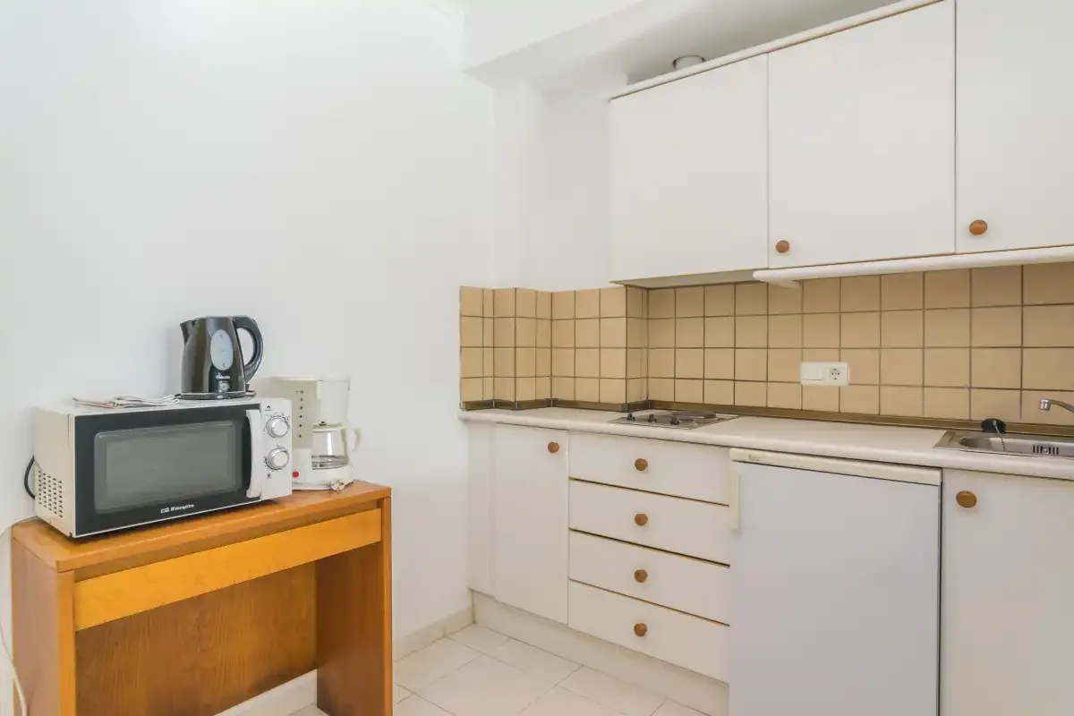 A compact kitchen with white cabinets, a tiled backsplash, and countertop appliances.