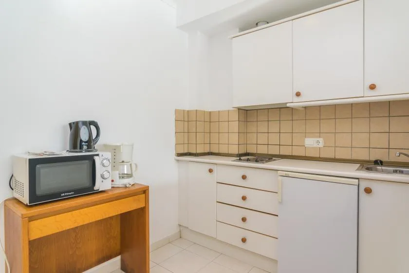 A compact kitchen with white cabinets, a tiled backsplash, and countertop appliances.