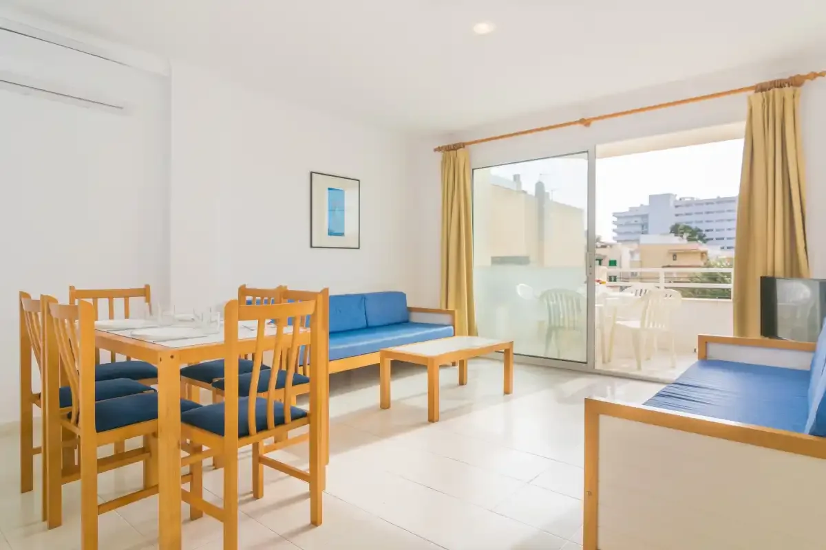 A bright living and dining area with wooden seating and glass doors opening onto a balcony.