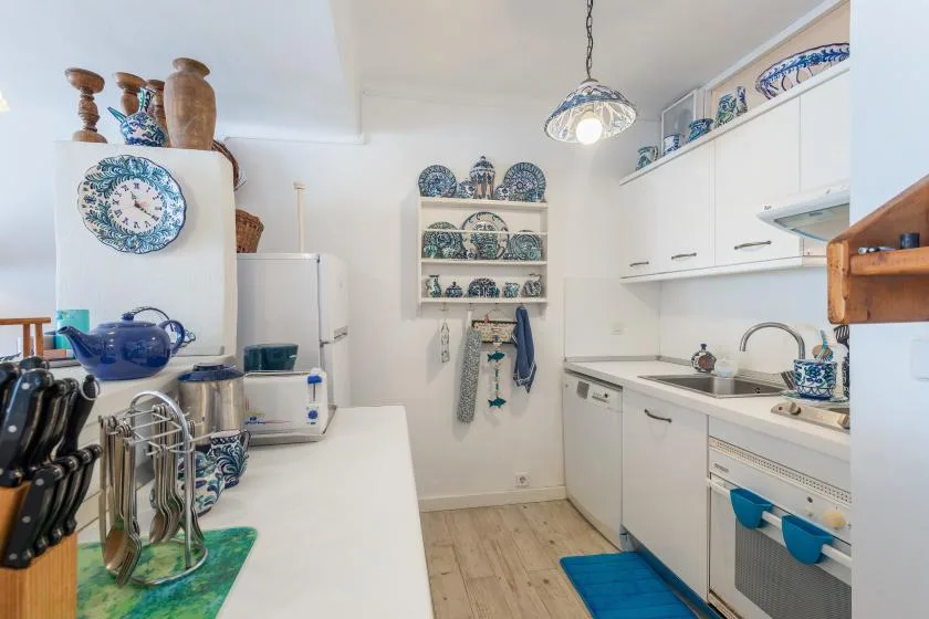 Una cocina luminosa con gabinetes blancos, una encimera larga y cerámica decorativa azul y blanca.