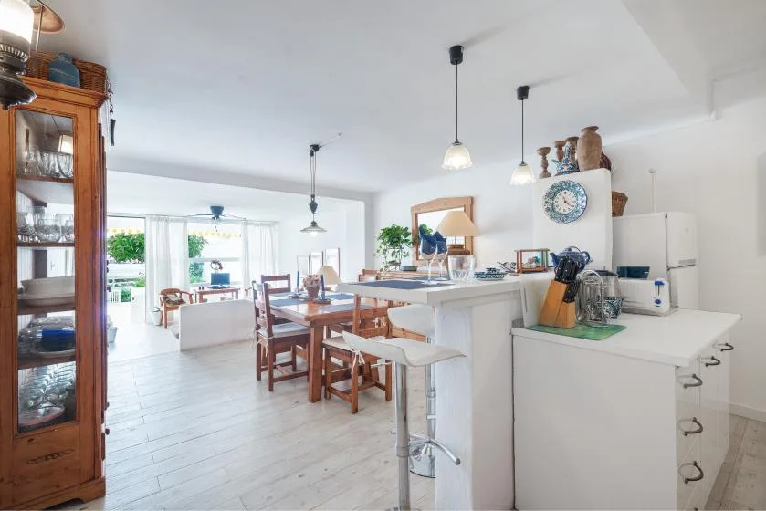 Una luminosa cocina abierta al comedor, con una encimera larga y una mesa de madera.