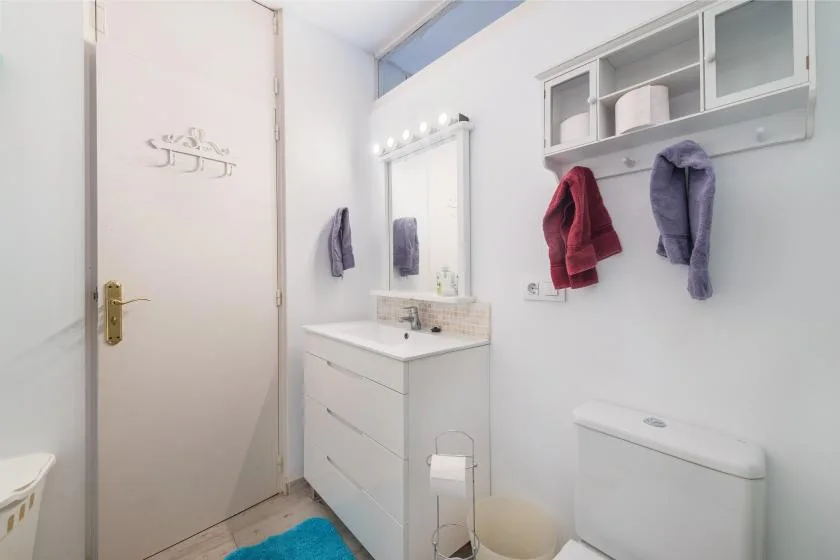 Un baño luminoso con lavabo, espejo y almacenamiento en la pared.