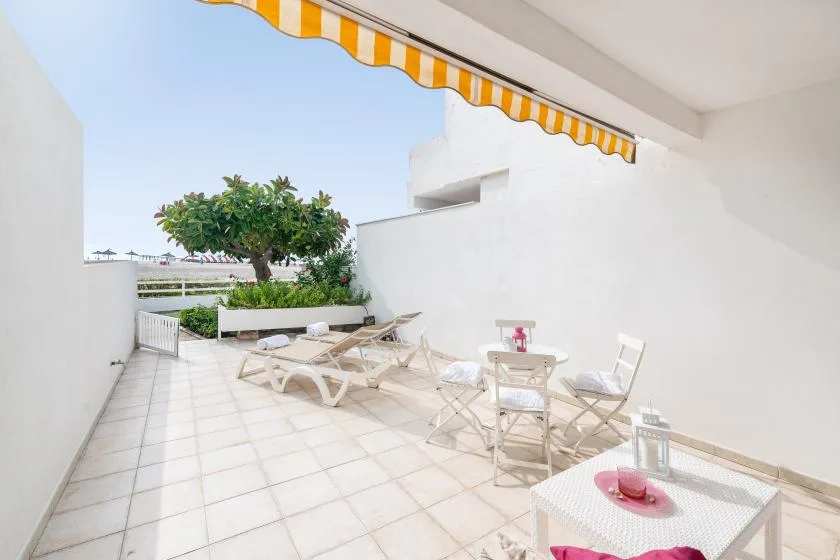 Una terraza exterior con suelo de baldosas, asientos y un toldo a rayas.