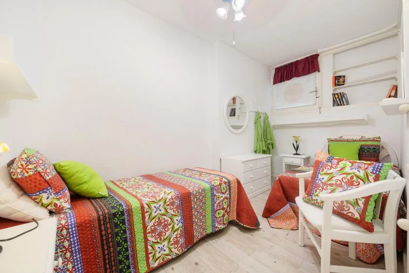 Un dormitorio colorido con ropa de cama estampada y una silla blanca junto a la cama.