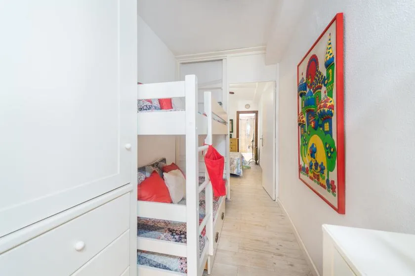 Un dormitorio estrecho con literas y una colorida obra enmarcada en la pared.