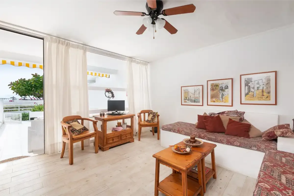 Una sala de estar luminosa con asientos de madera, una mesa baja y un televisor.