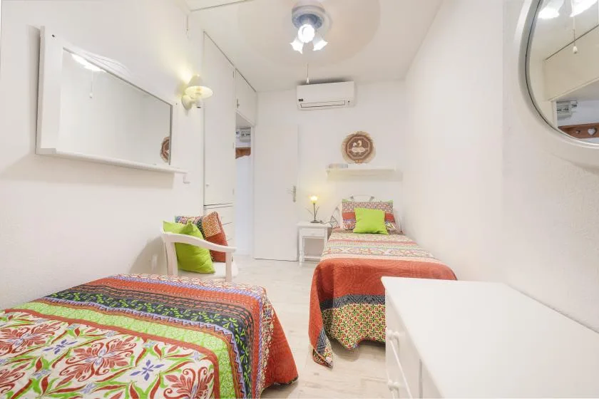 Un dormitorio luminoso con dos camas vestidas con ropa de cama estampada y colorida.