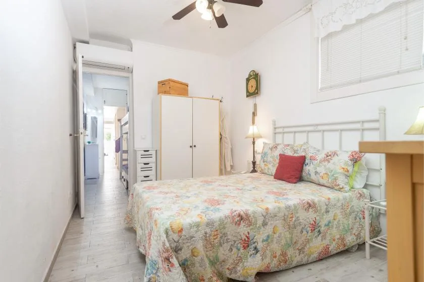 Un dormitorio con colcha floral, cabecero blanco y armario.