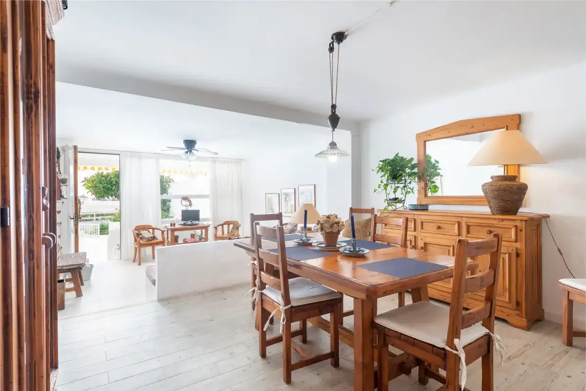 Comedor con una mesa de madera y sillas junto a una luminosa sala de estar.