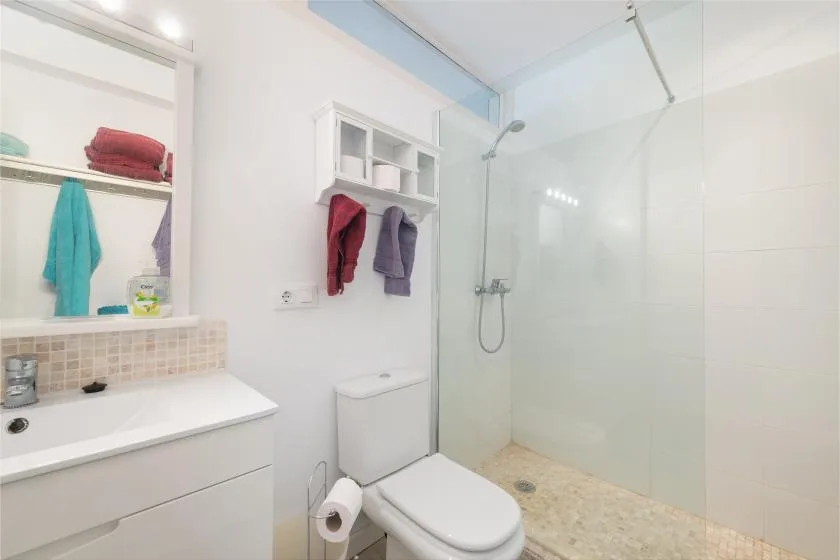 Un baño luminoso con lavabo, inodoro y ducha de vidrio.