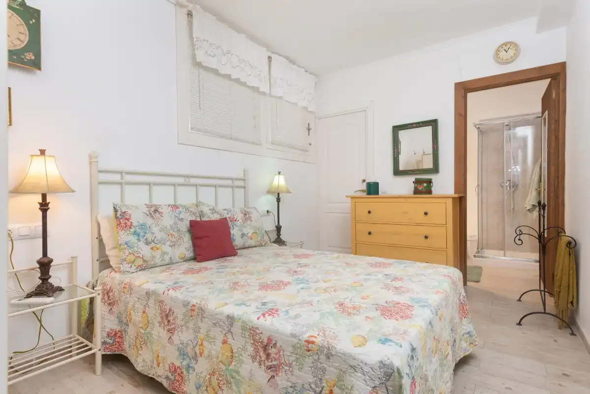Un dormitorio con ropa de cama floral, lámparas de noche y una cómoda de madera.