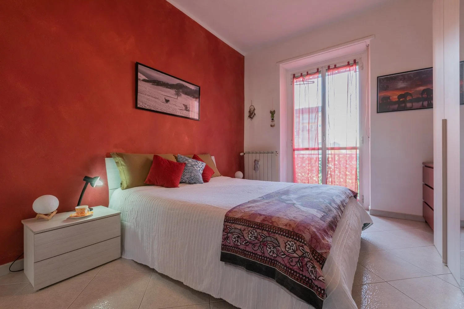 Un dormitorio con una cama, ropa de cama colorida y una puerta acristalada al balcón.