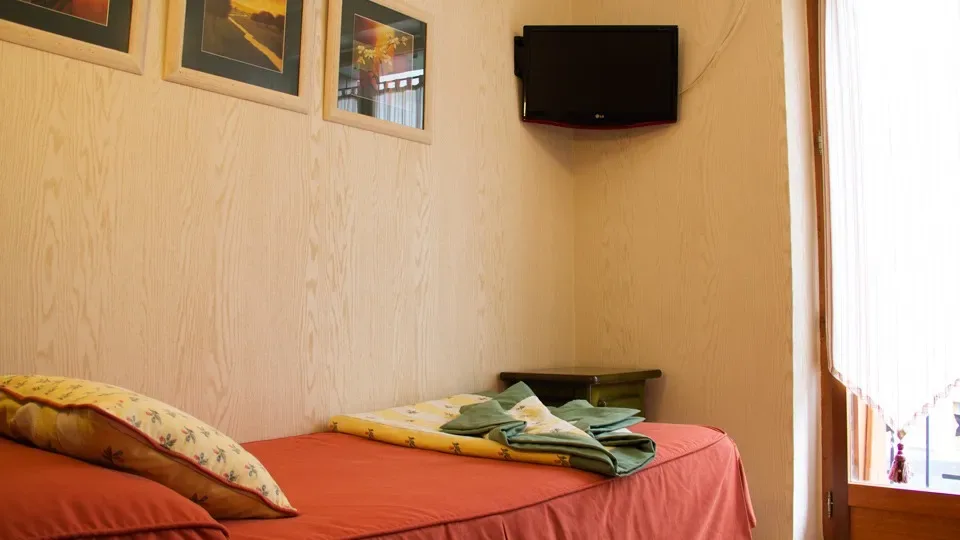 Habitación pequeña de hotel con una cama individual y televisor.