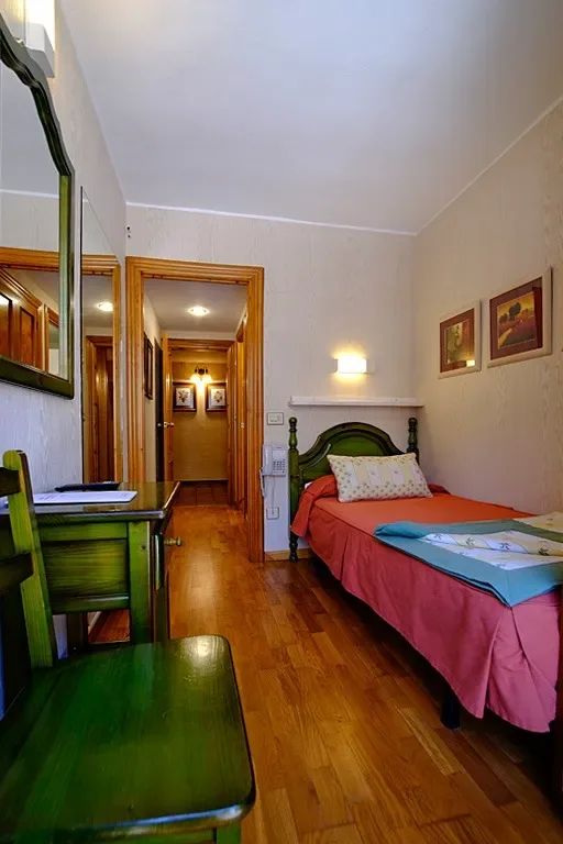 Habitación pequeña de hotel con una cama individual, escritorio y pasillo.
