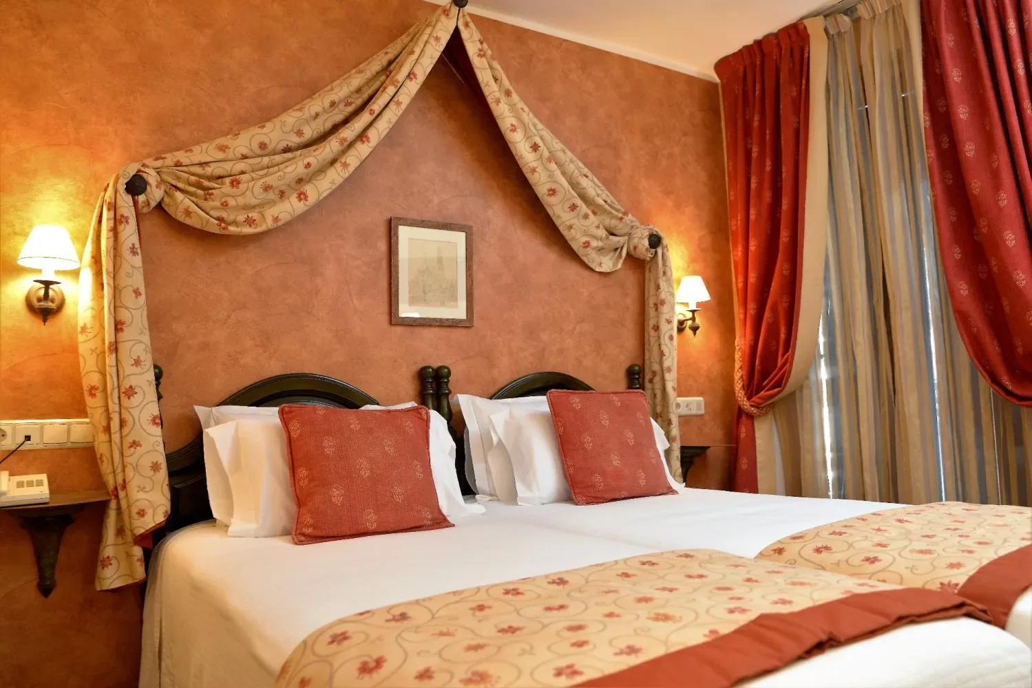 Dormitorio de hotel con una cama con dosel y detalles rojos y dorados.