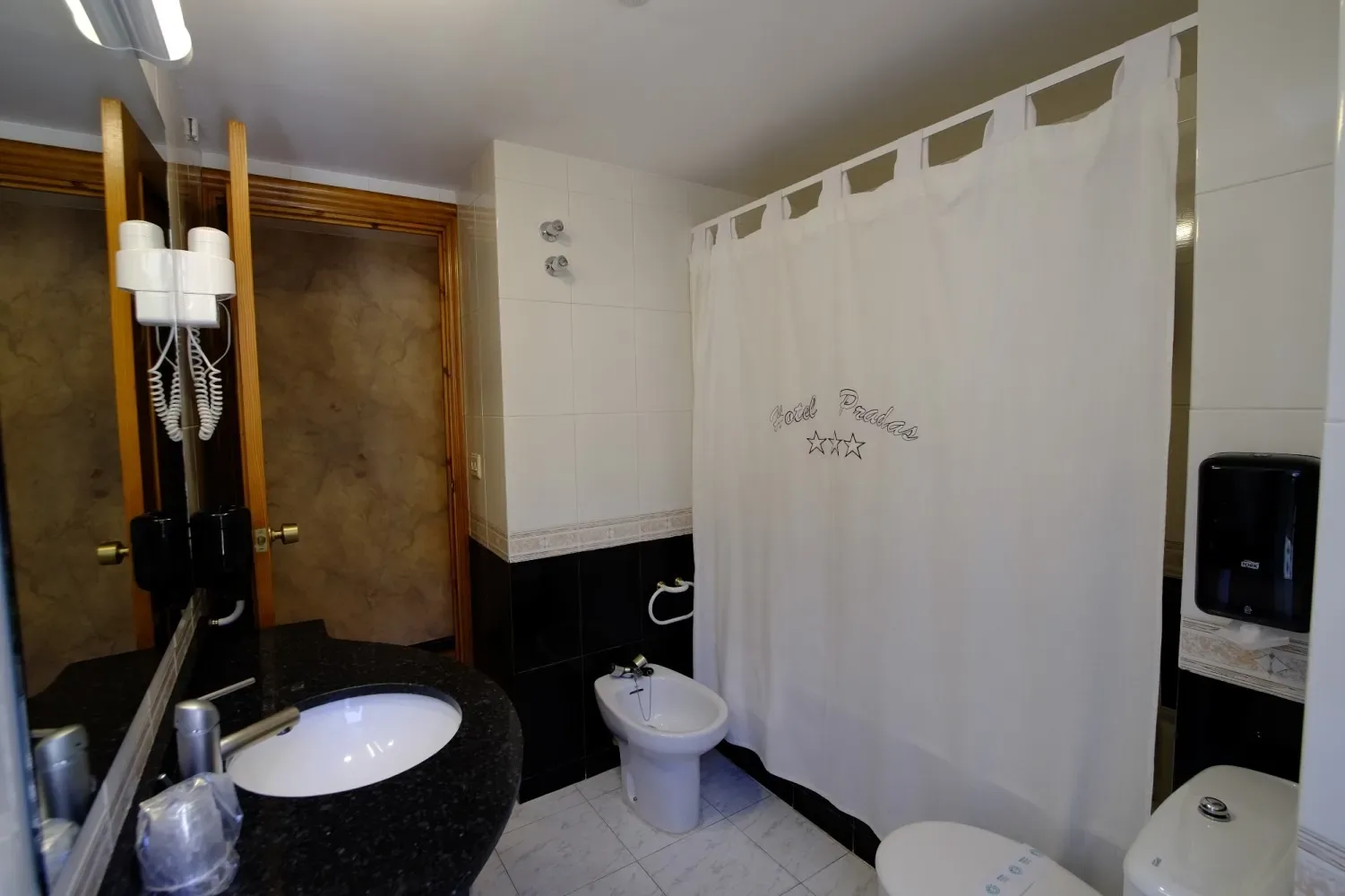 Baño con azulejos blancos y negros, lavabo, inodoro y cortina de ducha.