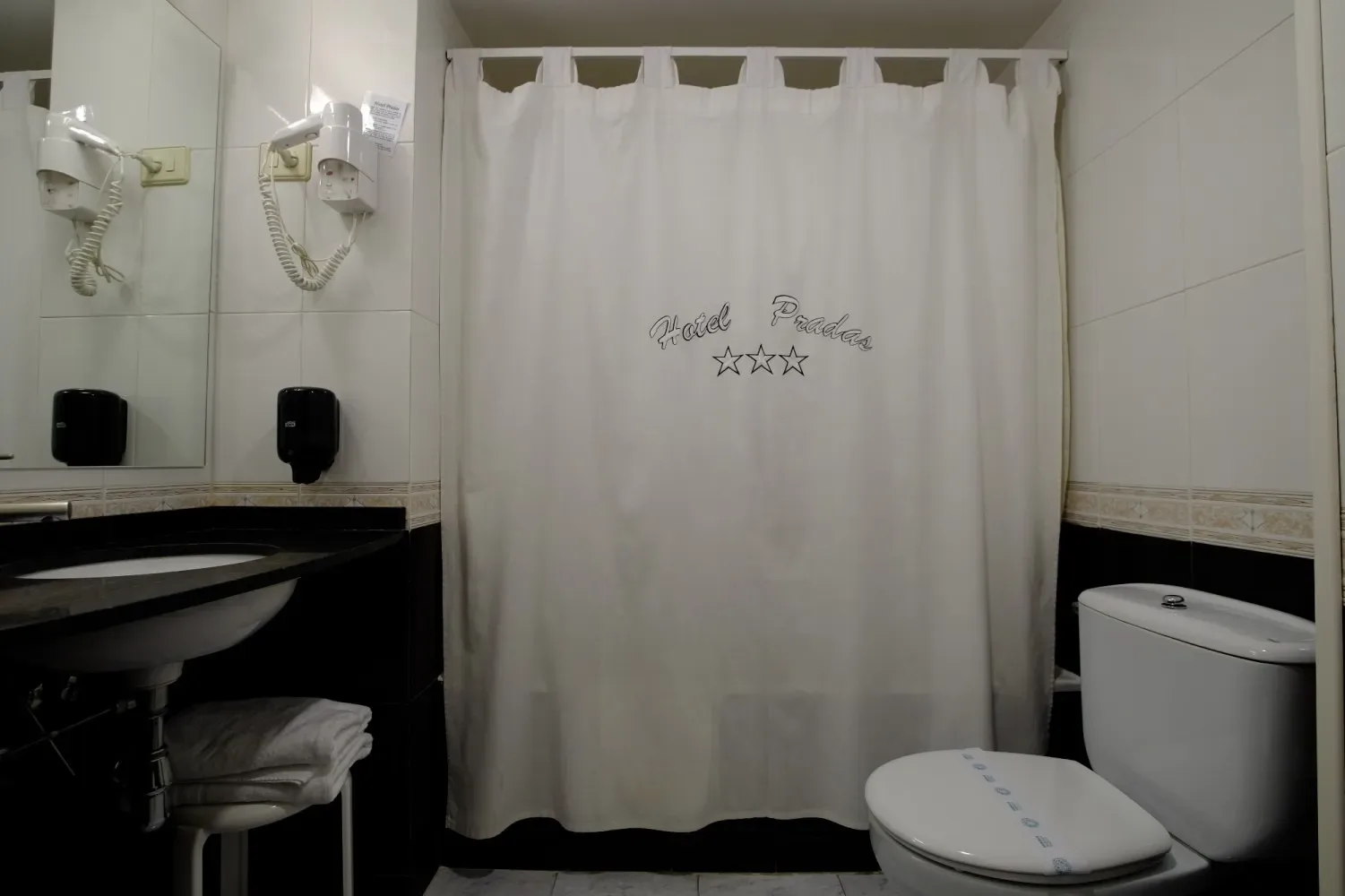 Baño con inodoro, lavabo, espejo y cortina de ducha.