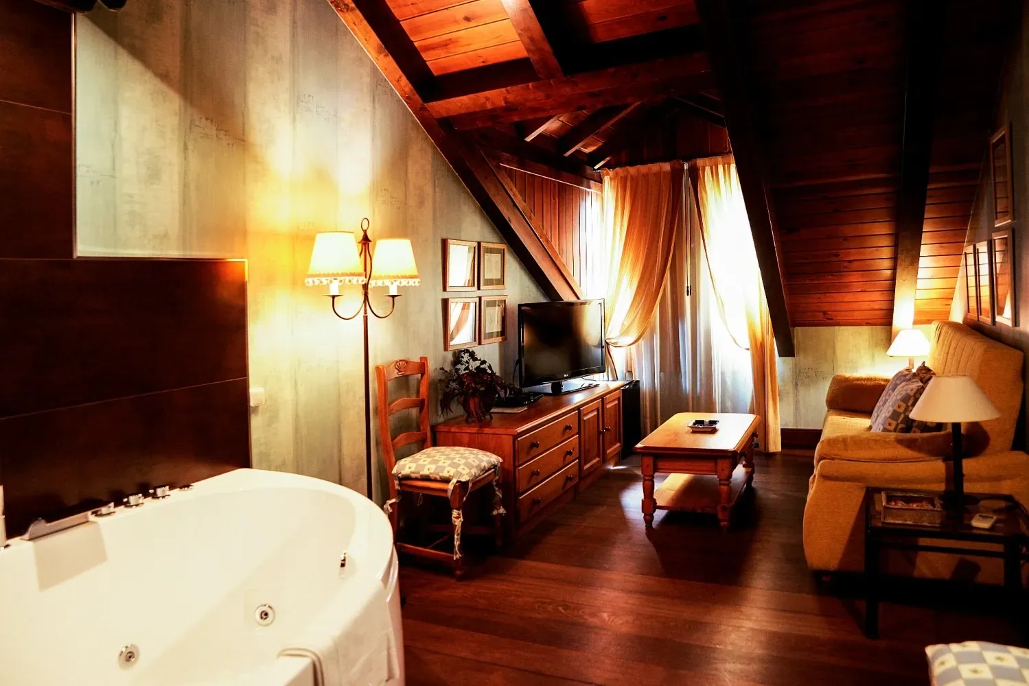 Habitación de hotel con jacuzzi, sofá, televisor y techo de madera.
