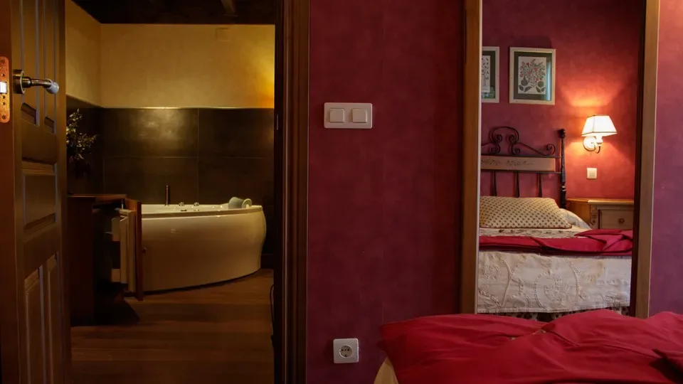 Dormitorio con pared roja, espejo y entrada a un baño.