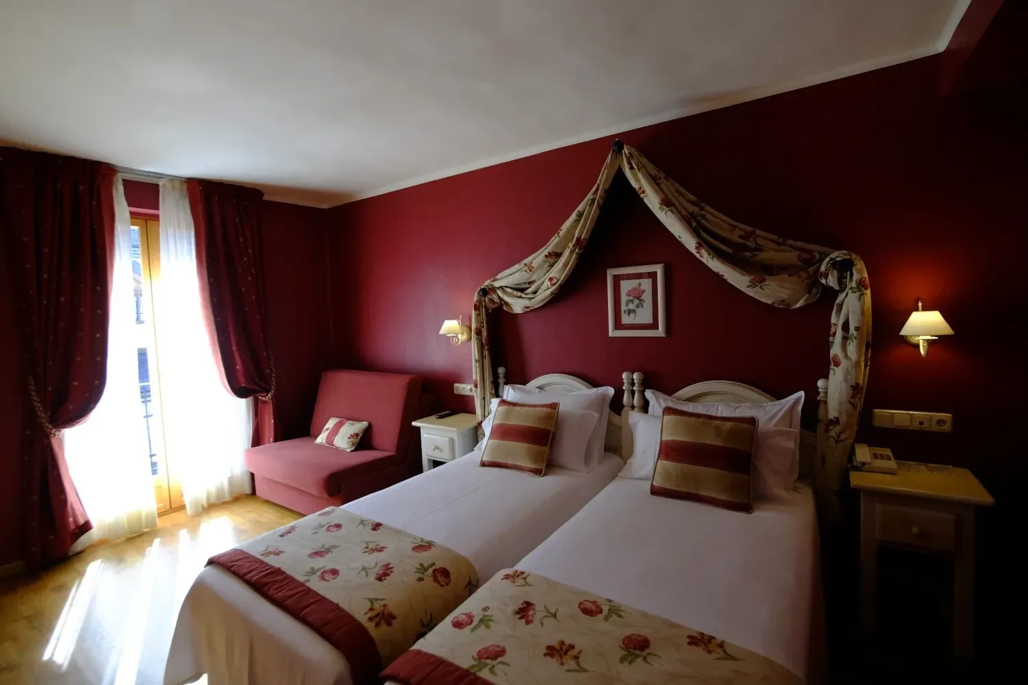 Habitación de hotel con dos camas individuales, paredes rojas y detalles de dosel.