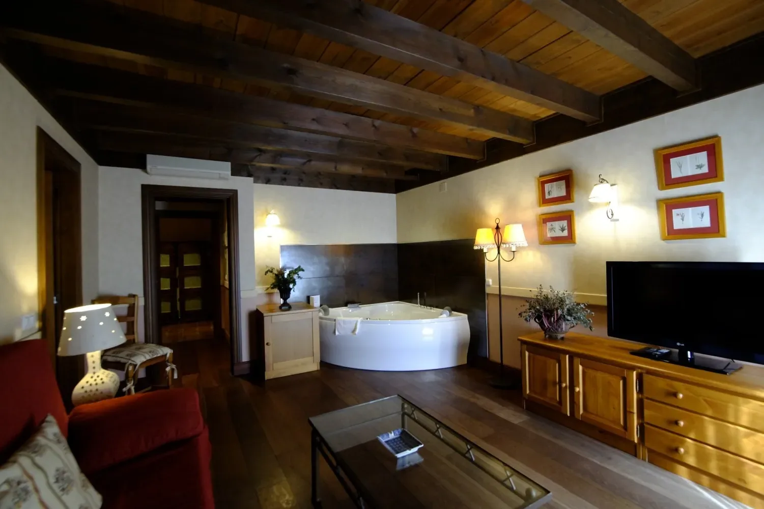 Habitación de hotel con techo de madera oscura, jacuzzi, sofá rojo y televisor.