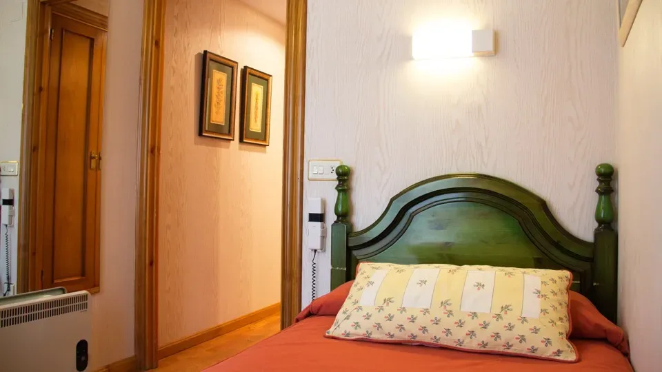 Dormitorio pequeño con una estructura de cama verde y ropa de cama de colores.