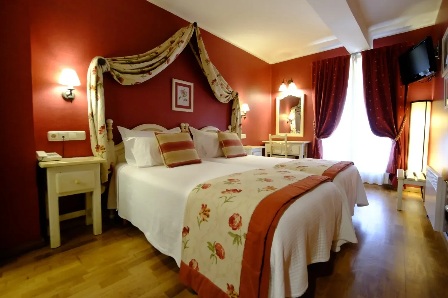 Dormitorio con pared roja, cama con dosel y ropa de cama blanca.