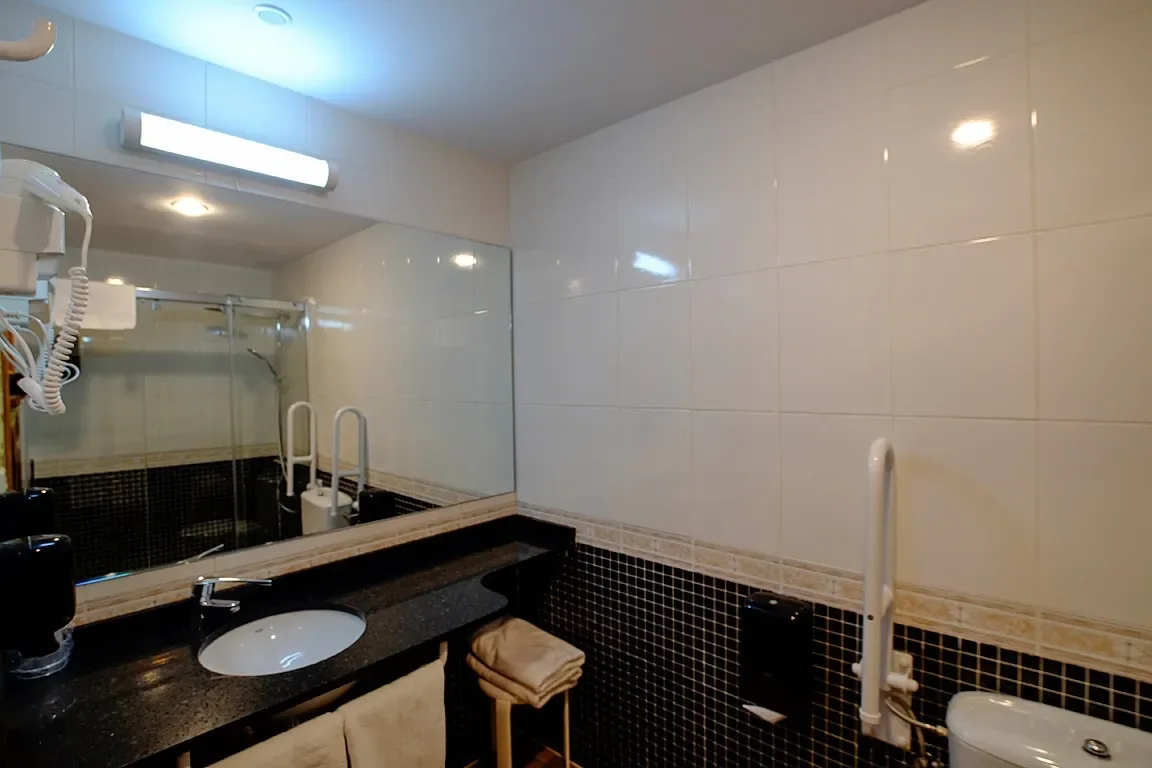 Baño con lavabo, espejo, inodoro y paredes alicatadas.
