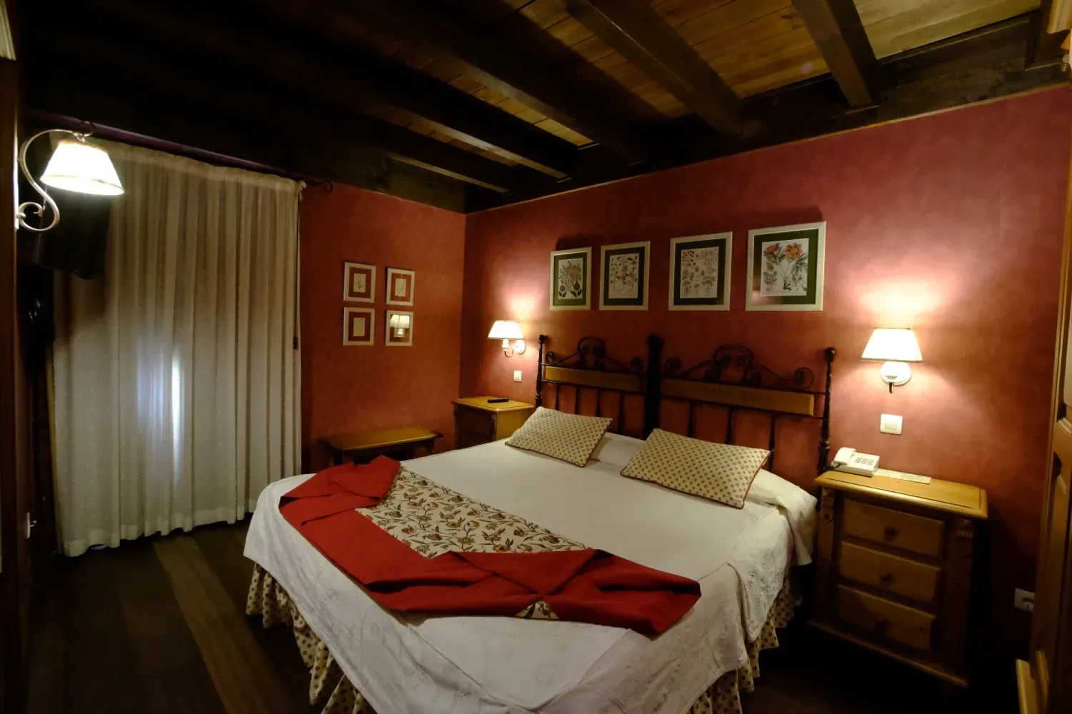 Dormitorio con paredes rojas, estructura de cama de madera y ropa de cama blanca.