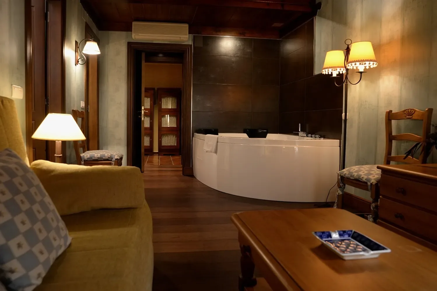 Habitación de hotel con jacuzzi, sofá y suelo de madera oscura.